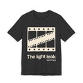 Dark gray t-shirt with a film reel design and white 'The light leak frame first' text on a white background