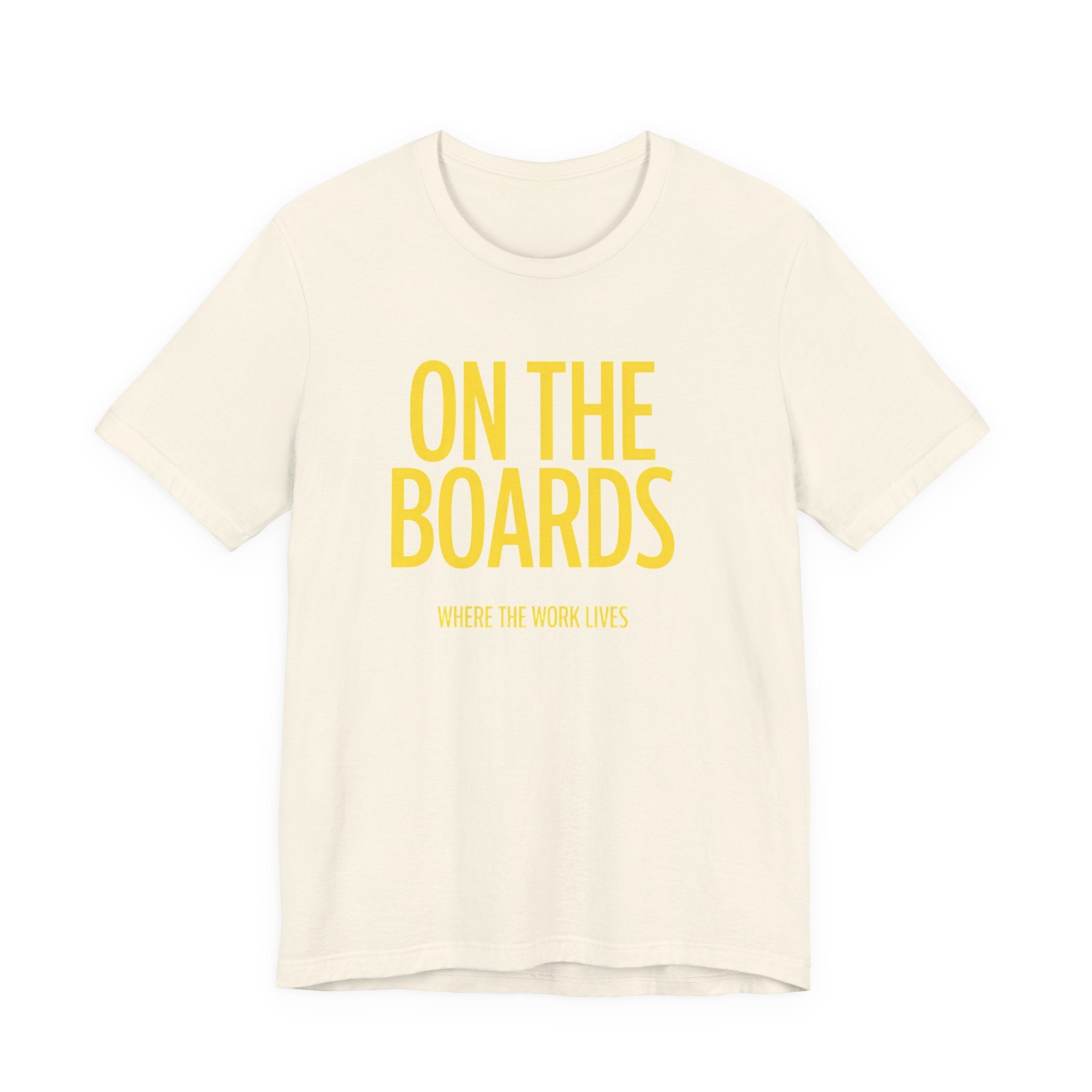 Beige t-shirt with yellow text 'ON THE BOARDS' on a white background
