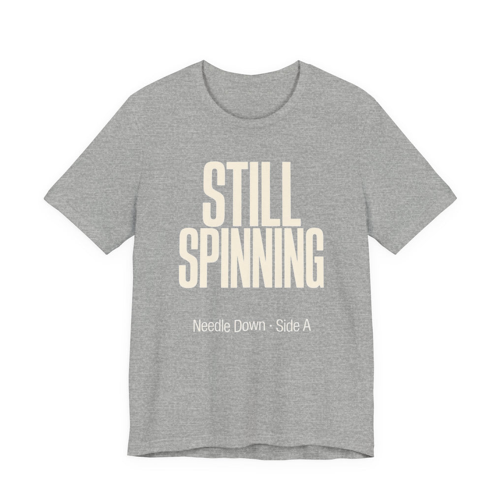 Gray t-shirt with 'STILL SPINNING' text on a white background