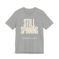 Gray t-shirt with 'STILL SPINNING' text on a white background
