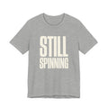 Gray t-shirt with 'STILL SPINNING' text on a white background