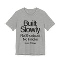 Gray t-shirt with black text 'Built Slowly No Shortcuts No Hacks Just Time' on a white background