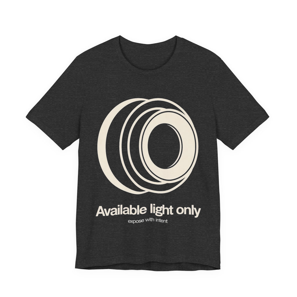 Dark gray t-shirt with white camera lens graphic and text 'Available light only' on a white background
