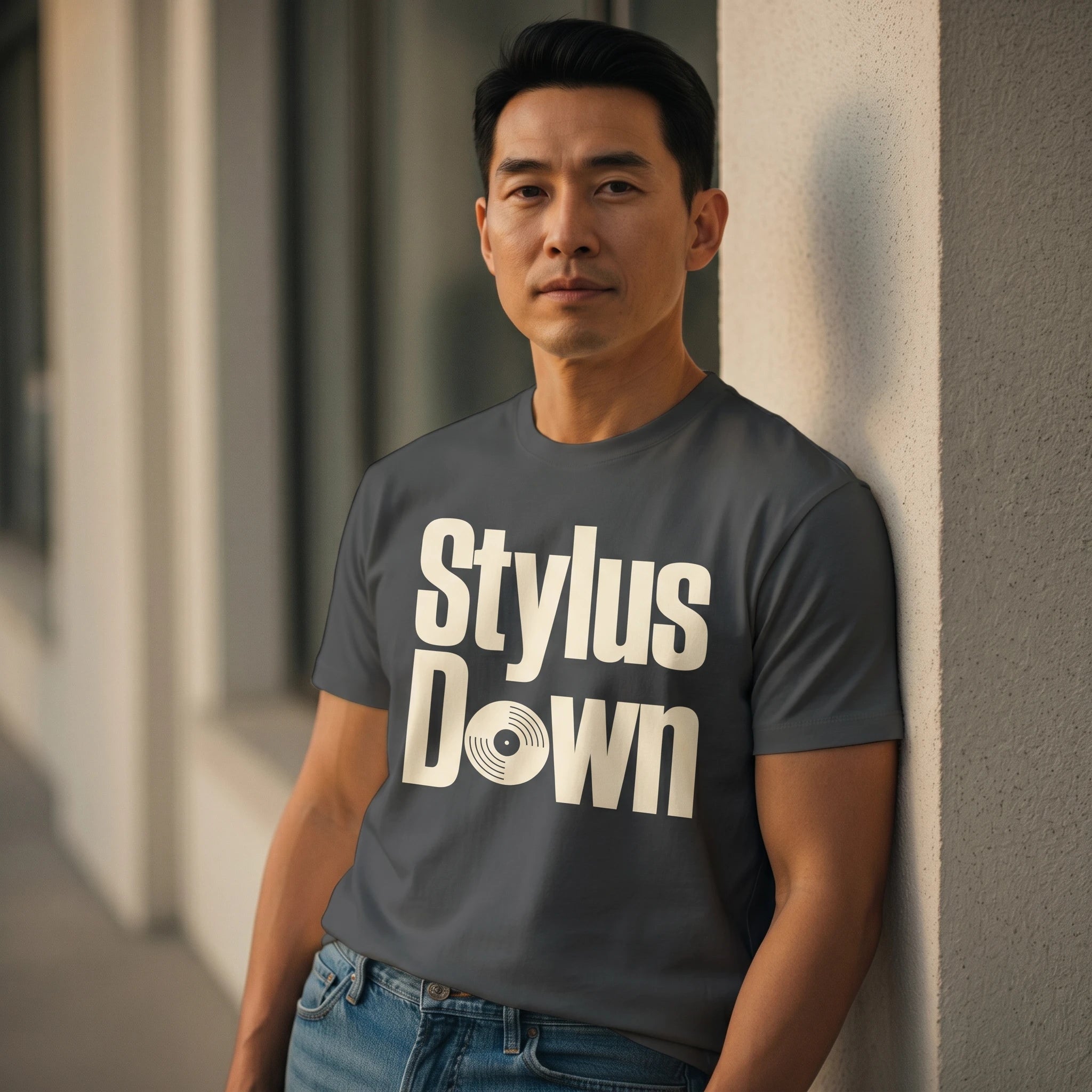 Man wearing a gray t-shirt with 'Stylus Down' text, leaning against a wall.