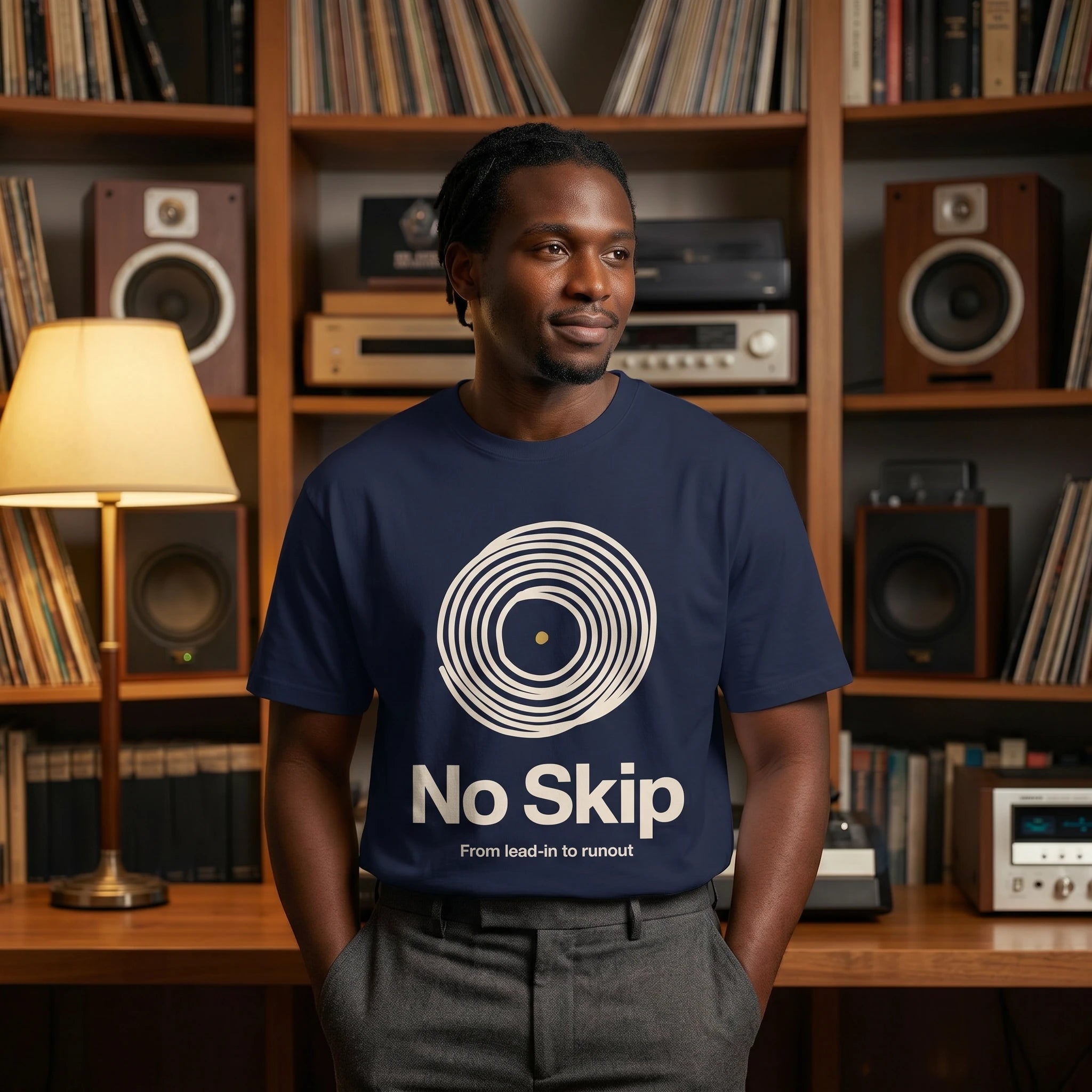 Man wearing a navy blue t-shirt with 'No Skip' design in a room with bookshelves and audio equipment.