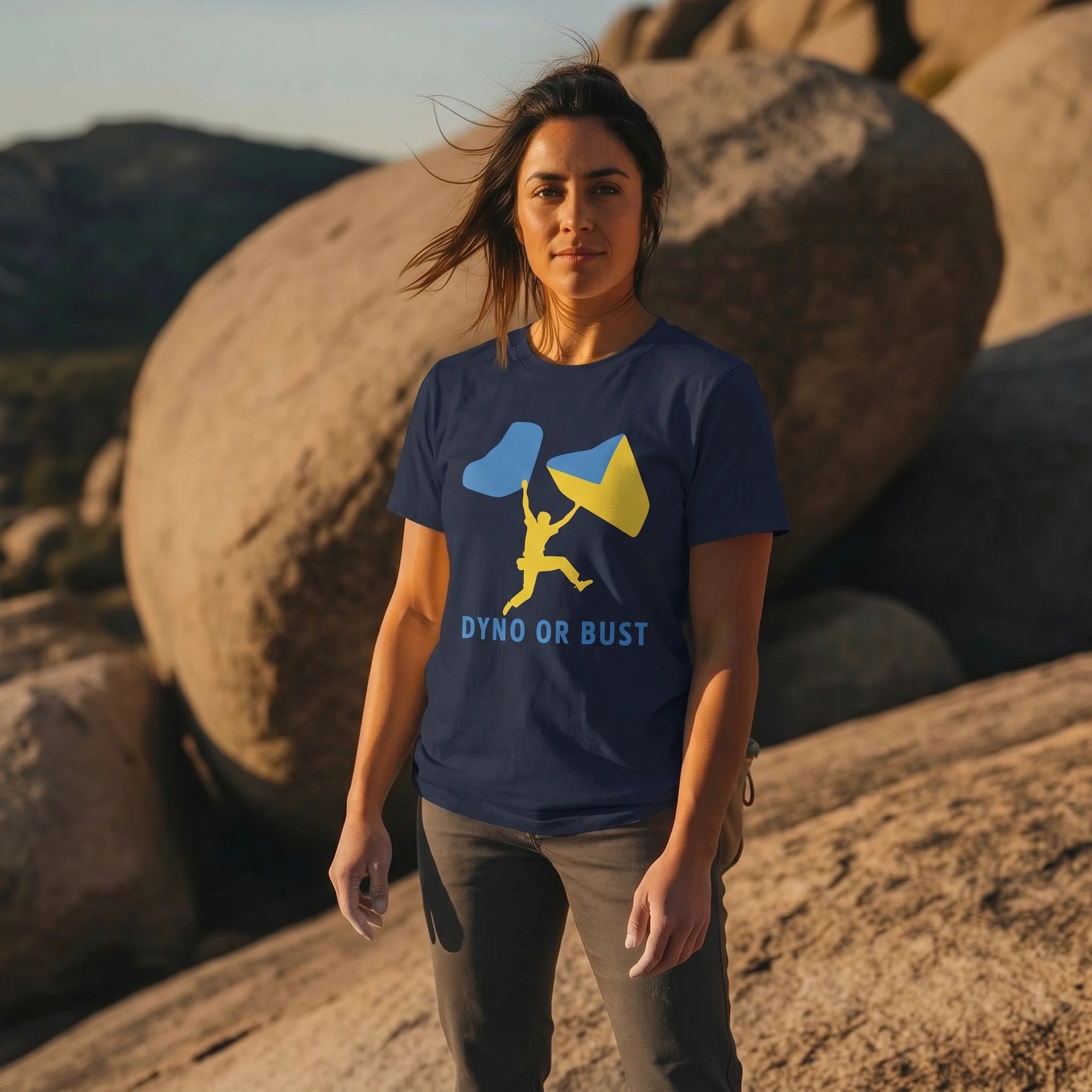Woman wearing a blue t-shirt with a graphic design and 'Dyno or Bust' text, standing in a rocky outdoor setting.