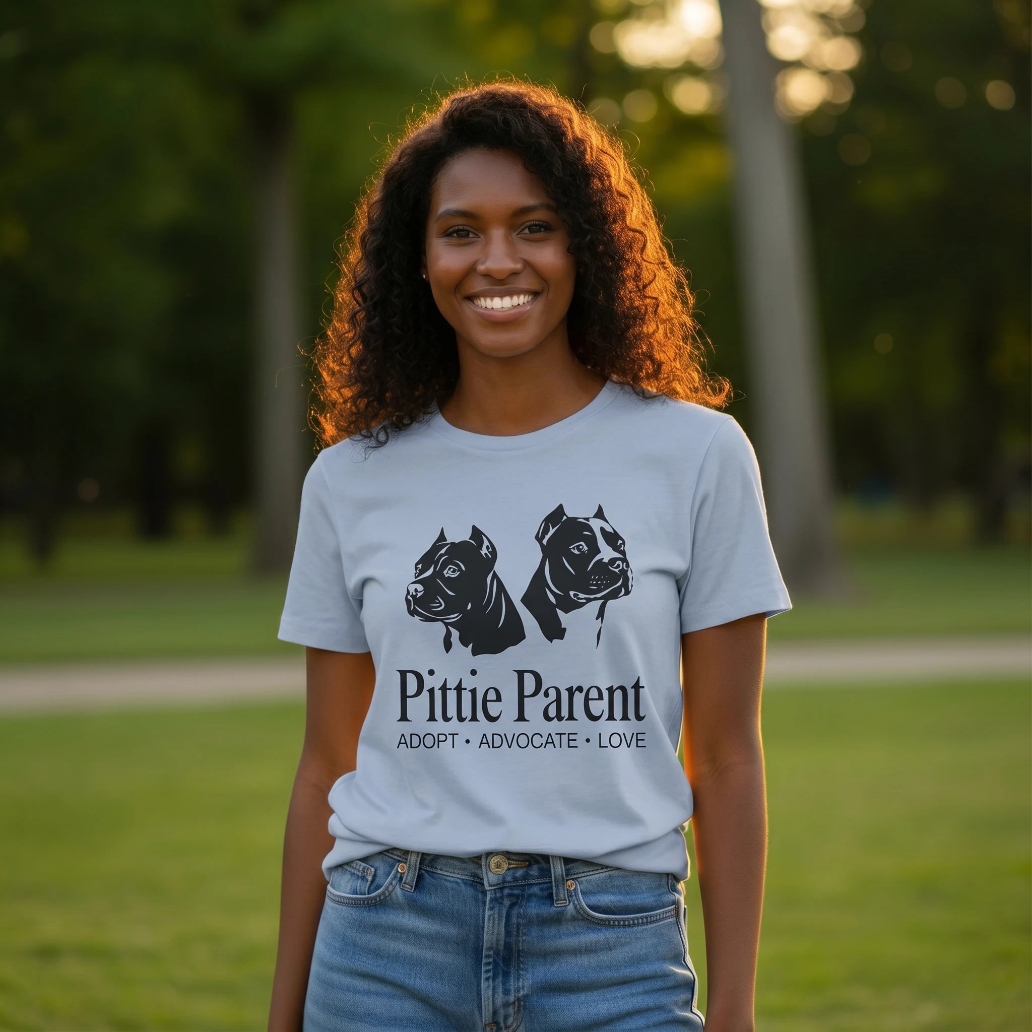 Woman wearing a 'Pittie Parent' t-shirt with dog illustrations in a park setting