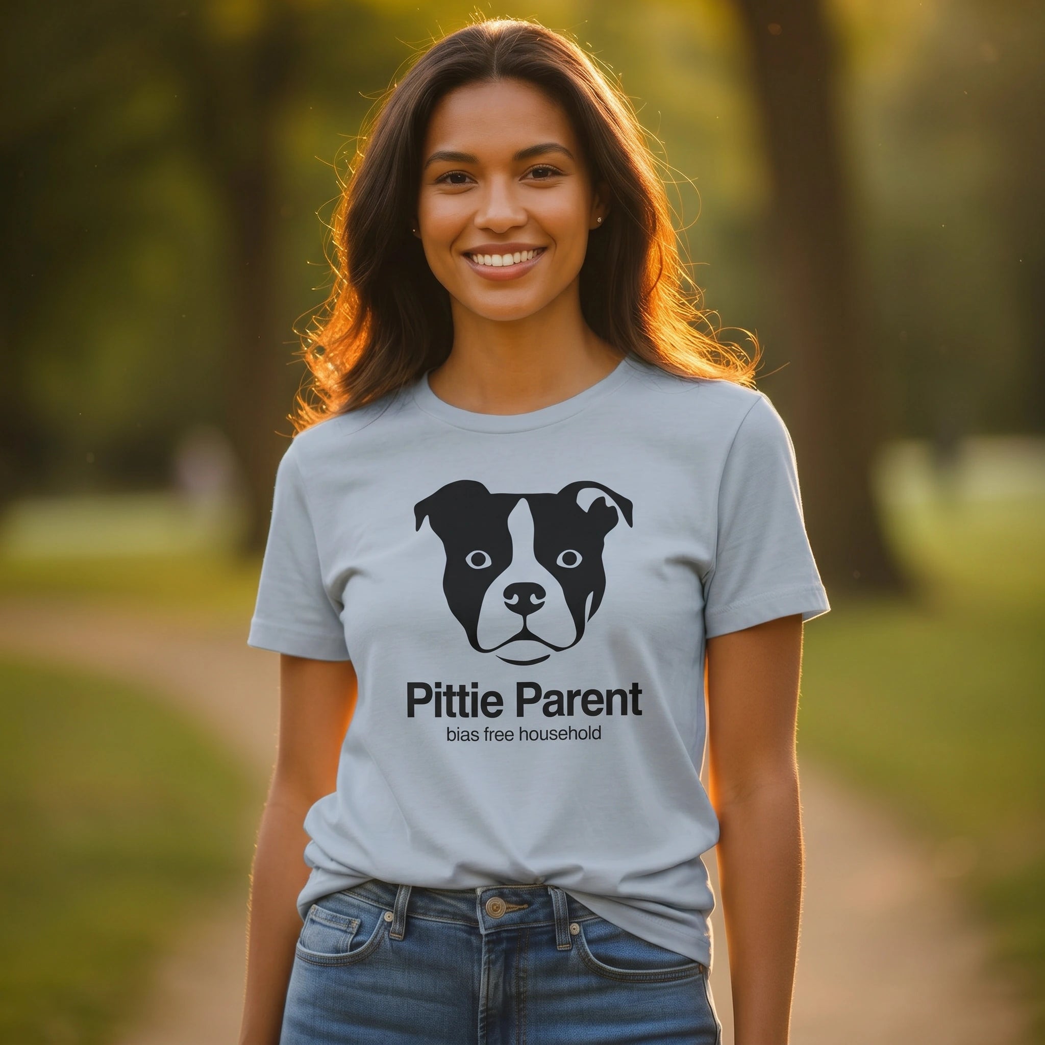 Woman wearing a light blue t-shirt with a black dog illustration and text 'Pittie Parent bias free household' text in a park
