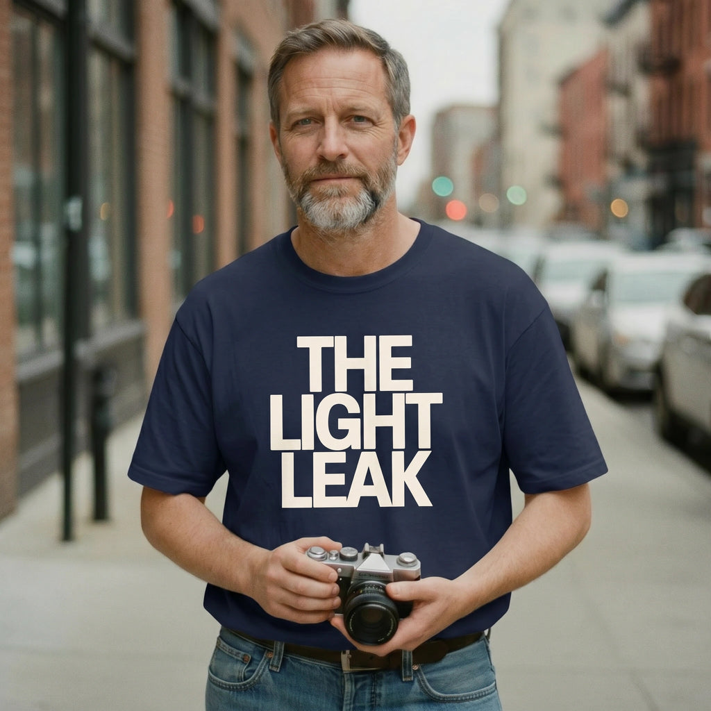 Man wearing a navy blue t-shirt with 'THE LIGHT LEAK' text, holding a camera on a city street.
