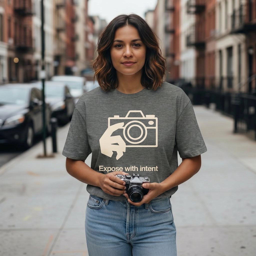 Woman holding a camera on a city street wearing a t-shirt with a camera graphic and text.