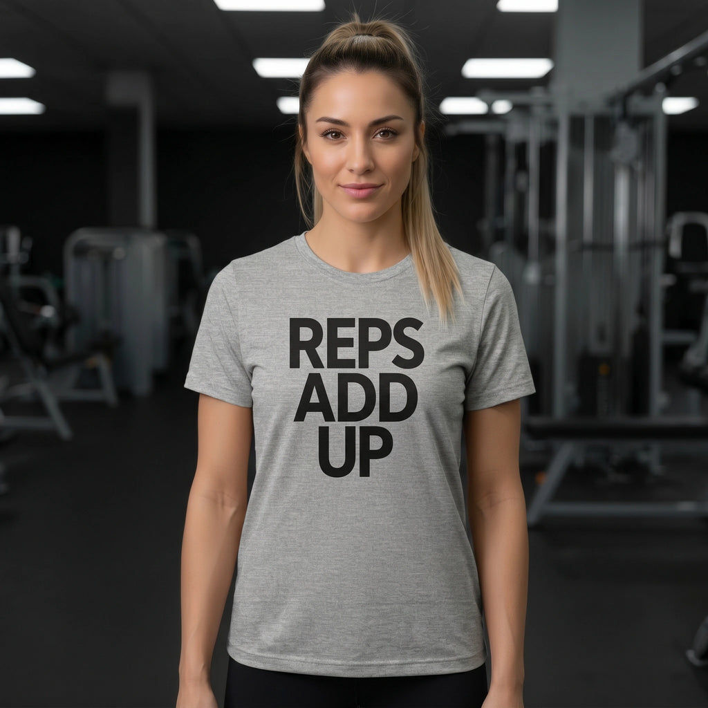 Woman wearing a gray t-shirt with 'REPS ADD UP' text in a gym setting
