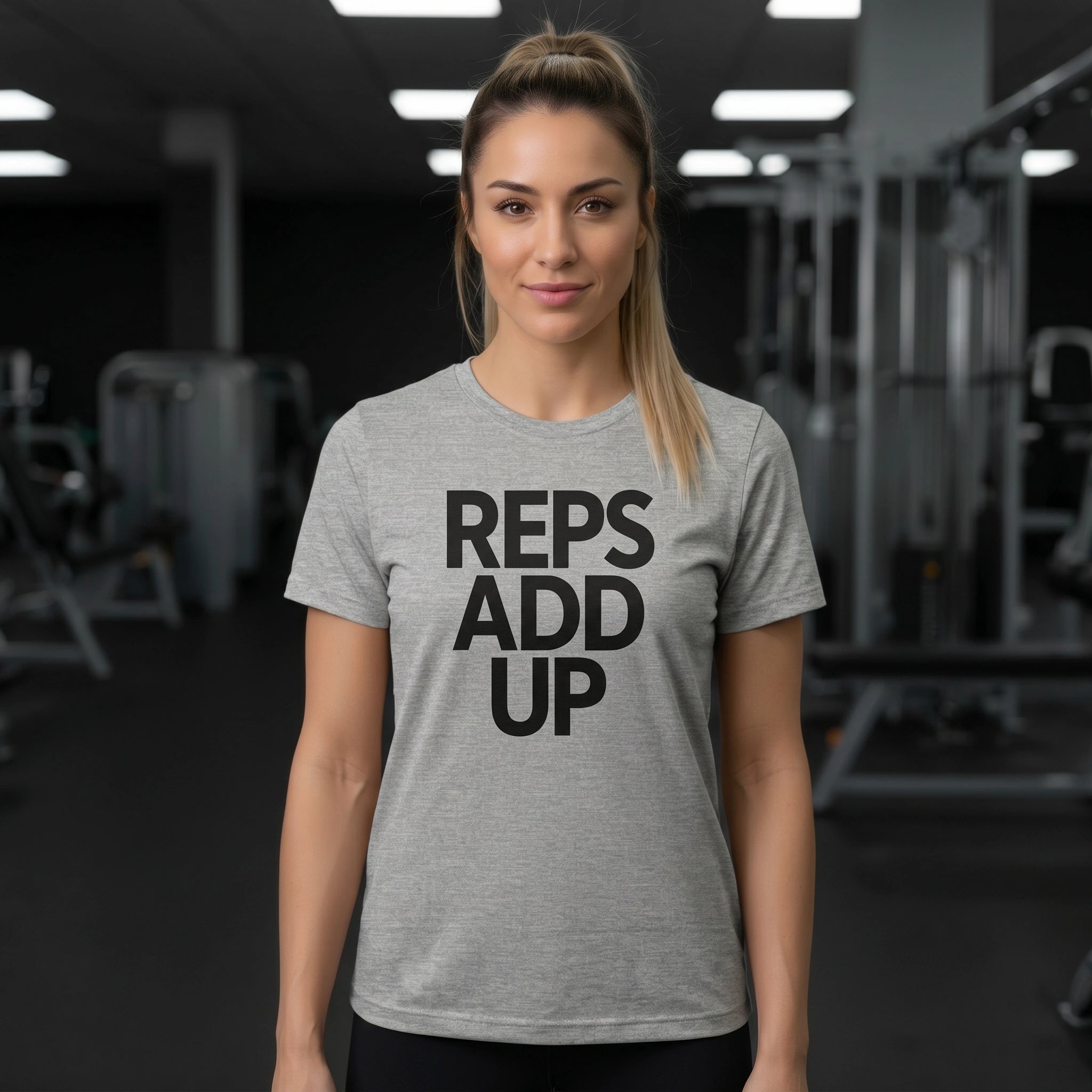 Woman wearing a gray t-shirt with 'REPS ADD UP' text in a gym setting