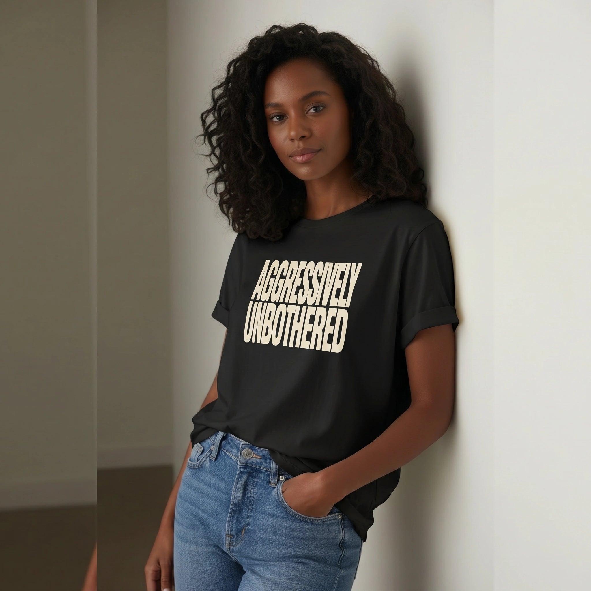 Woman wearing a black t-shirt with 'AGGRESSIVELY UNBOTHERED' text, standing against a neutral wall.