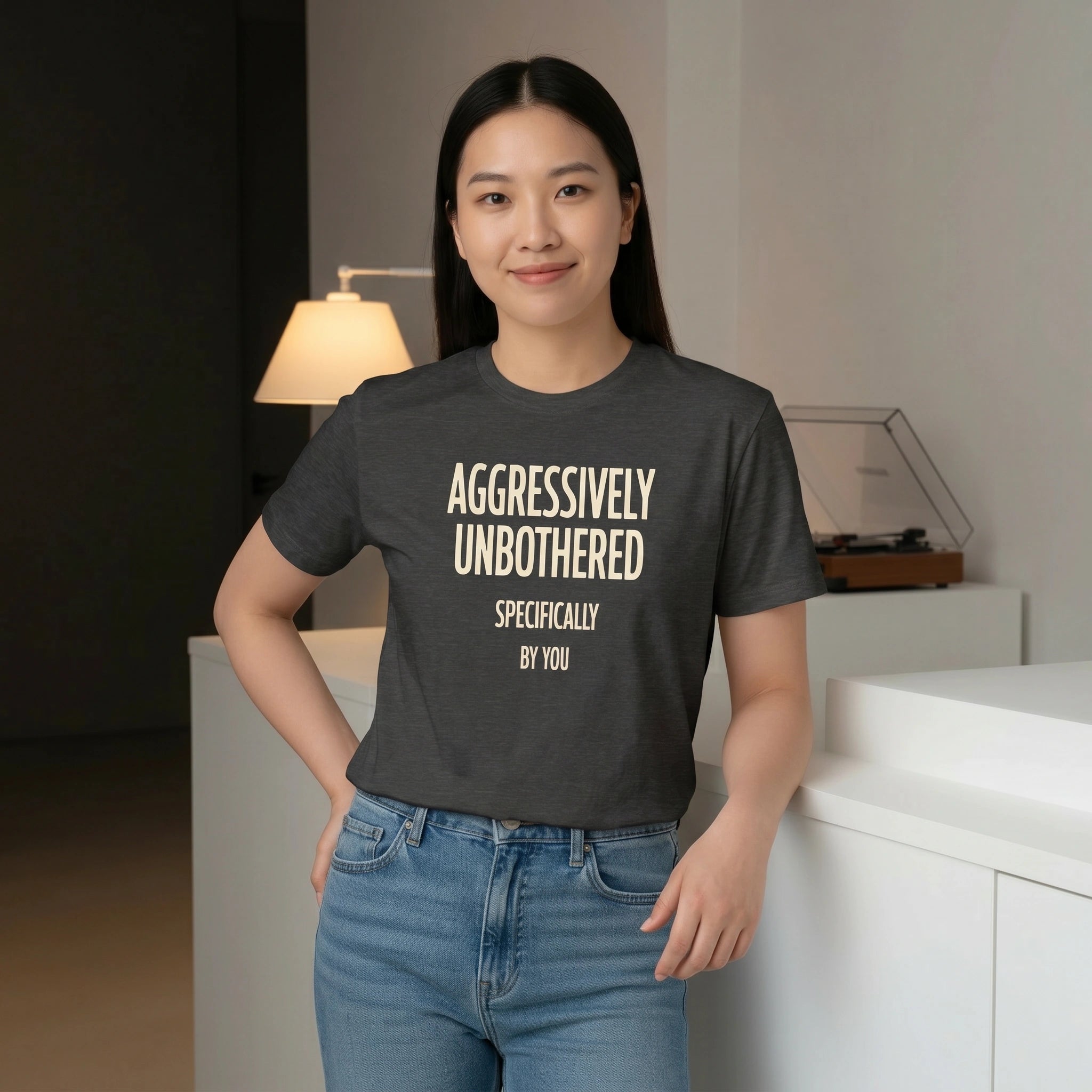 Person wearing a dark gray t-shirt with 'AGGRESSIVELY UNBOTHERED SPECIFICALLY BY YOU' text in a room.