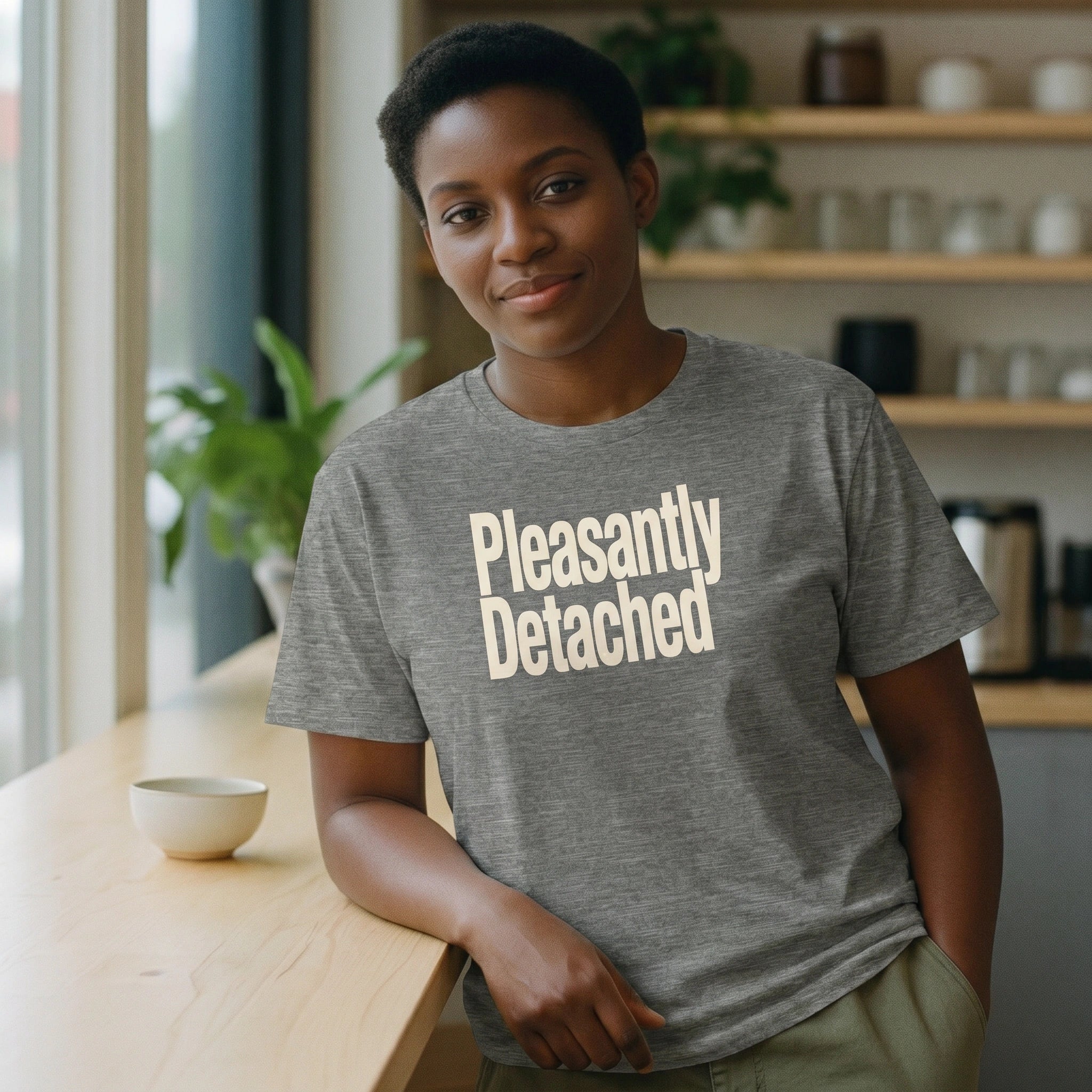 Person wearing a gray t-shirt with 'Pleasantly Detached' text in a casual setting.