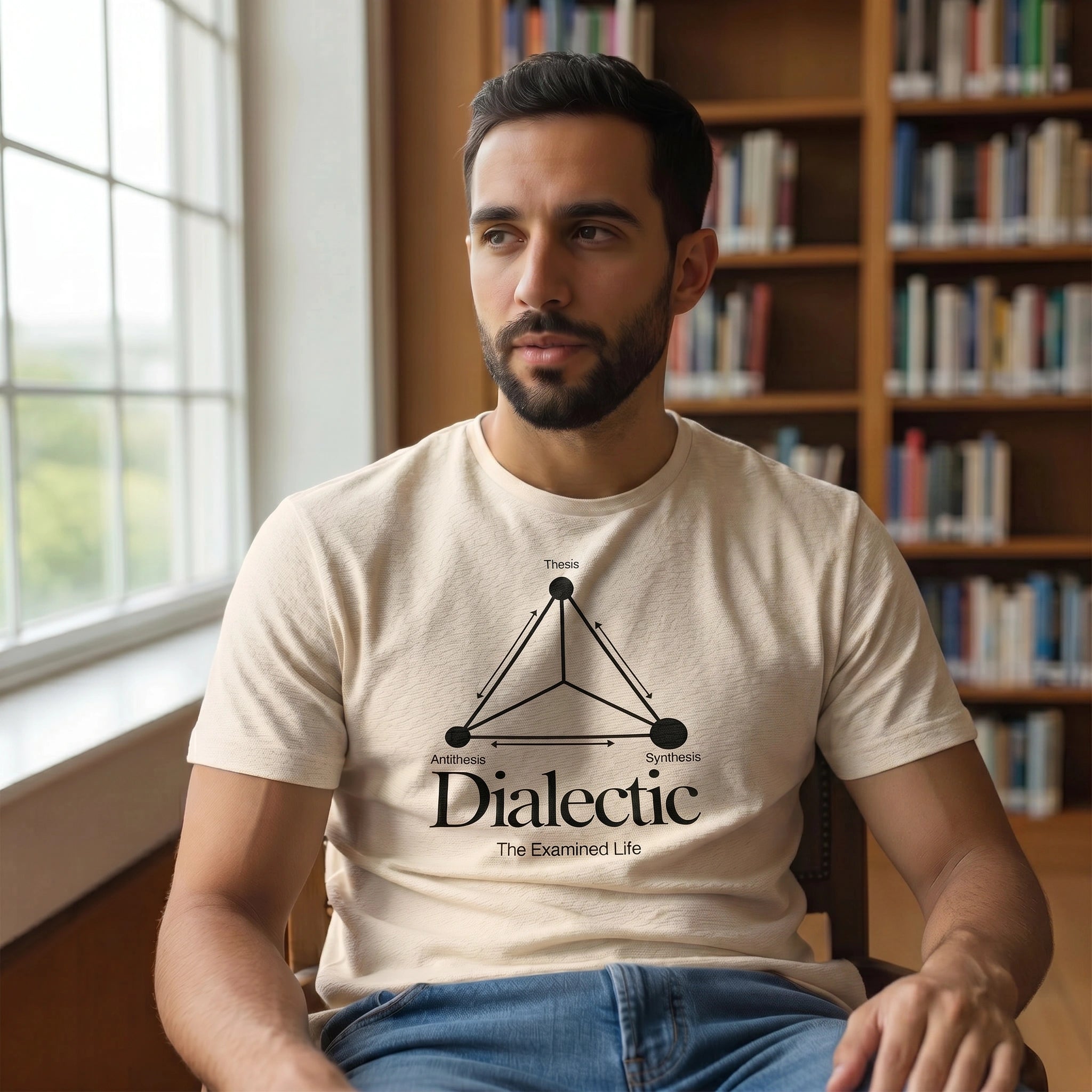 Man wearing a t-shirt with a graphic design sitting in a room with bookshelves.