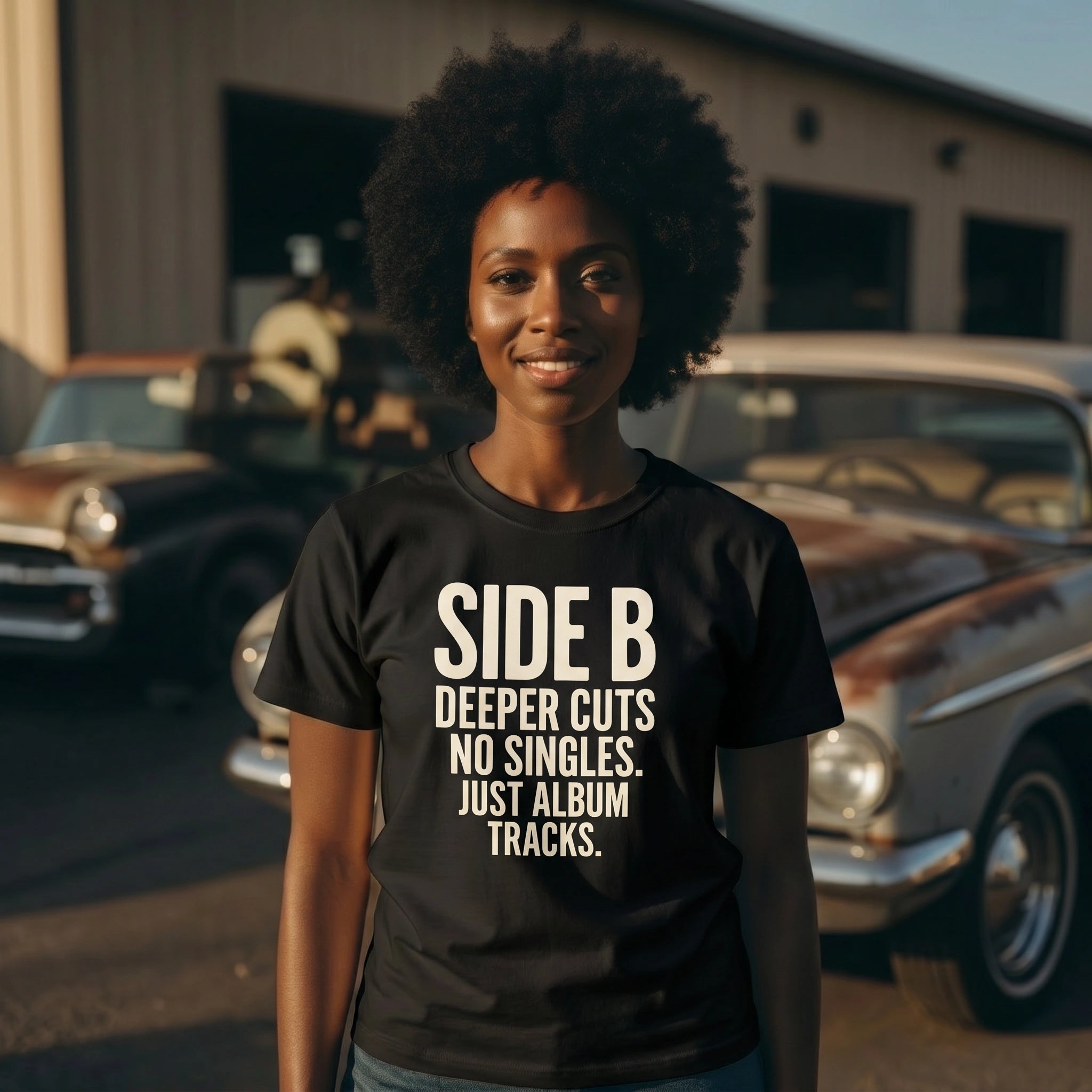 Person wearing a black t-shirt with text standing in front of vintage cars.