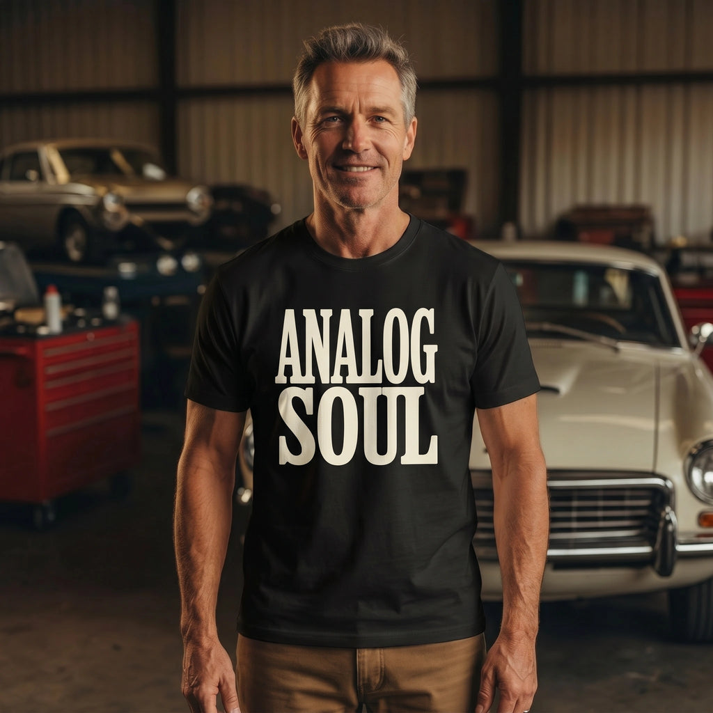 Man wearing a black t-shirt with 'ANALOG SOUL' text in a garage with vintage cars.