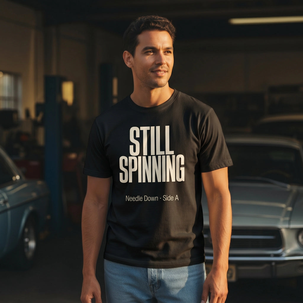 Man wearing a black t-shirt with 'STILL SPINNING' text in a garage setting