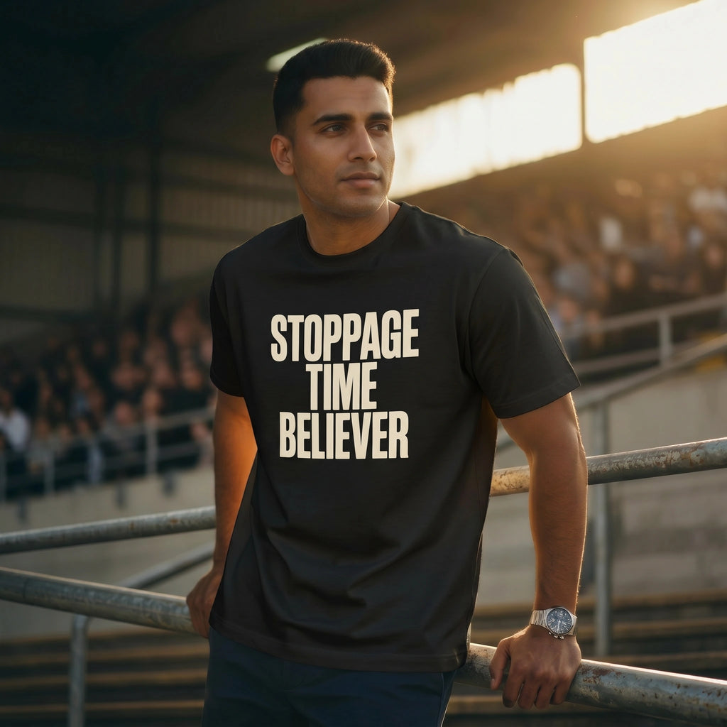 Man wearing a black t-shirt with 'STOPPAGE TIME BELIEVER' text in a stadium setting