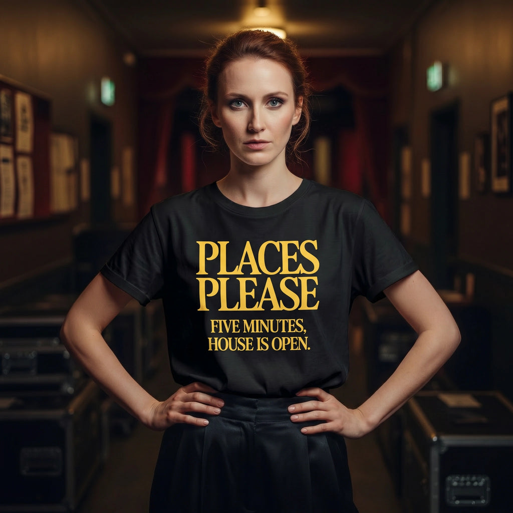 Woman wearing a black t-shirt with yellow 'Places Please' text in a dimly lit room.