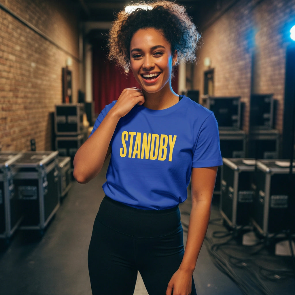 Person wearing a blue 'STANDBY' t-shirt in a backstage area with equipment.