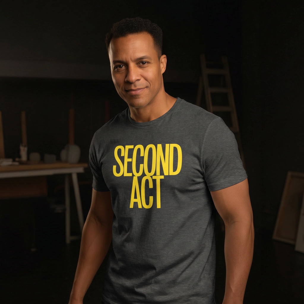 Man wearing a gray t-shirt with 'SECOND ACT' in yellow text, standing in a dark room.