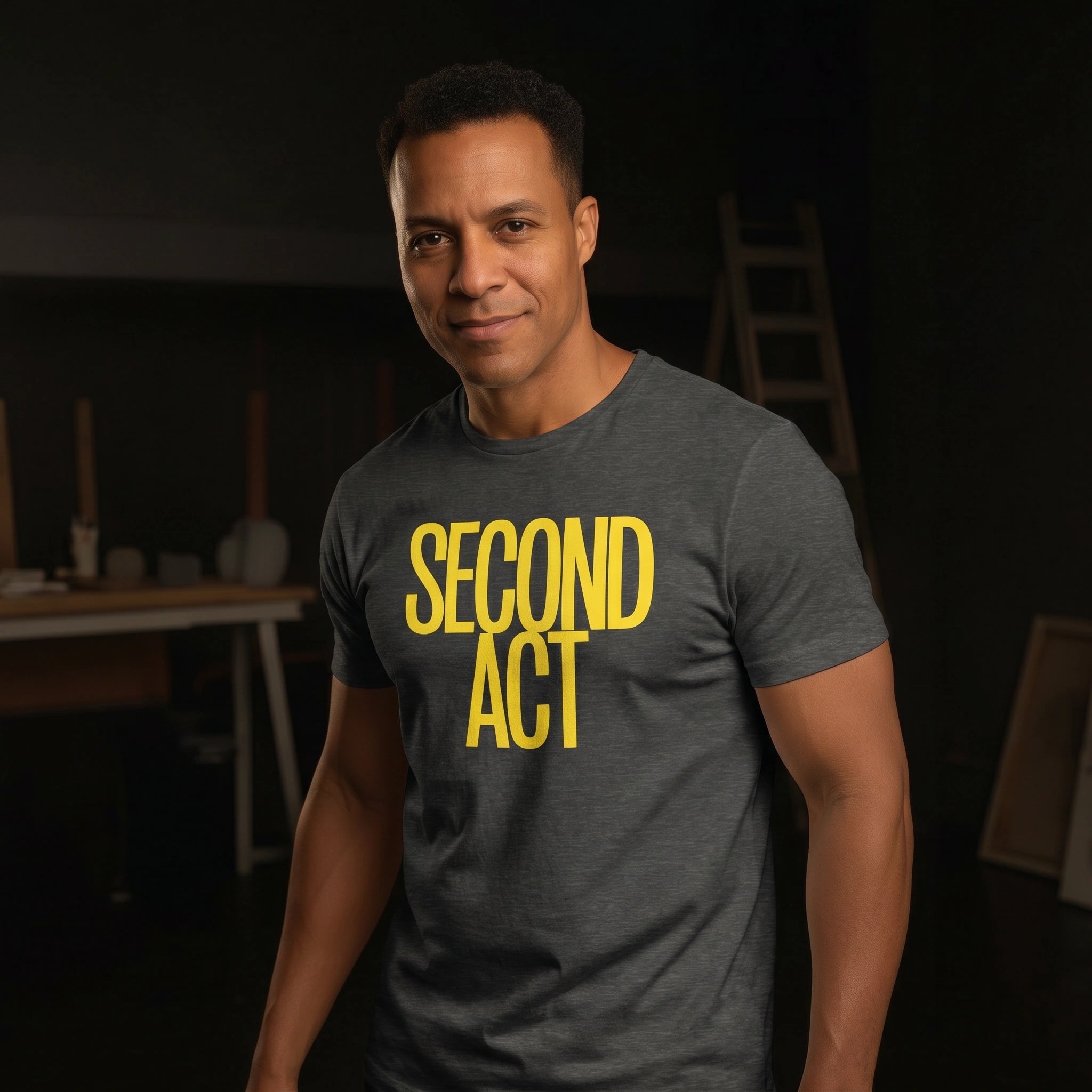 Man wearing a gray t-shirt with 'SECOND ACT' in yellow text, standing in a dark room.