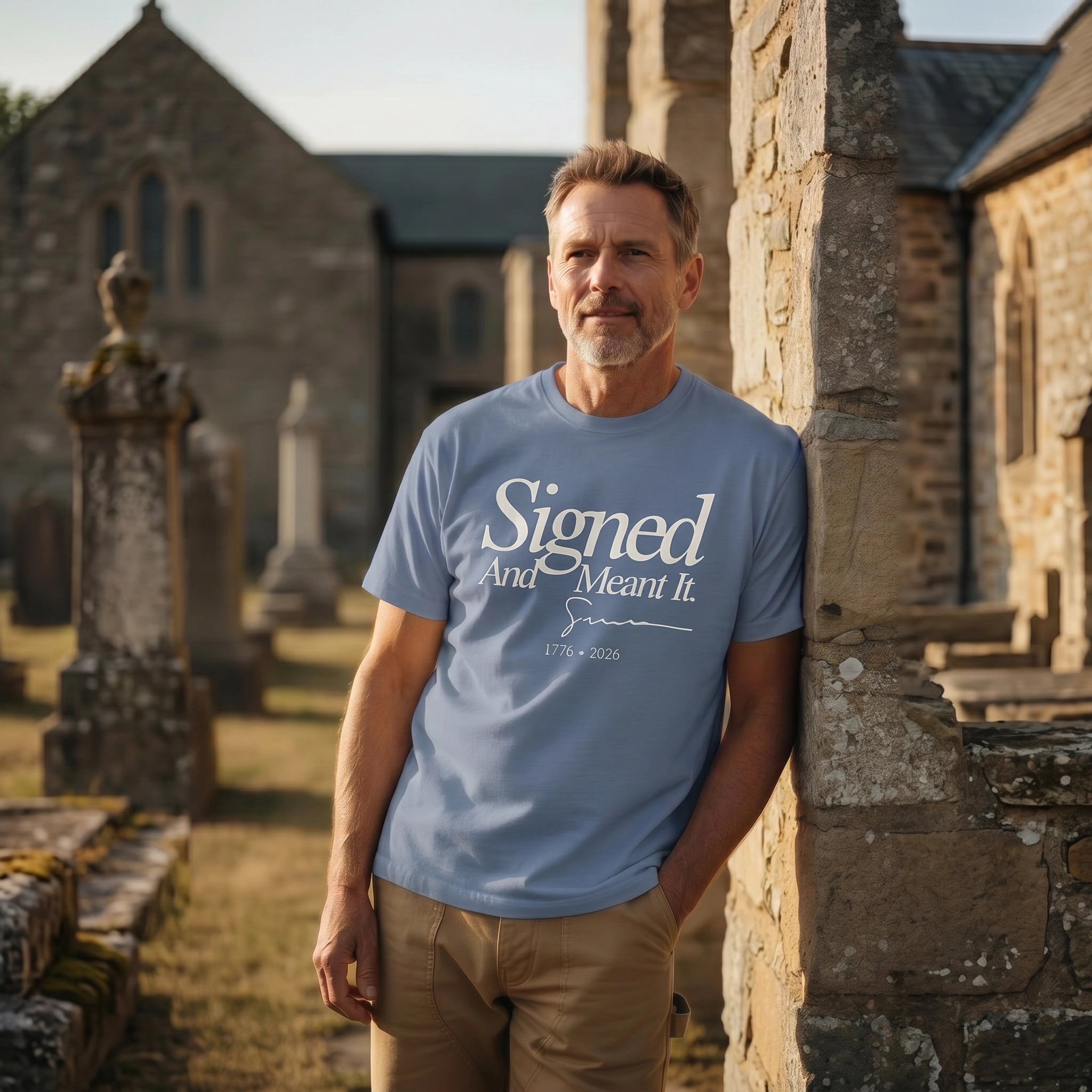 Man wearing a blue t-shirt with text standing in front of stone buildings and gravestones.